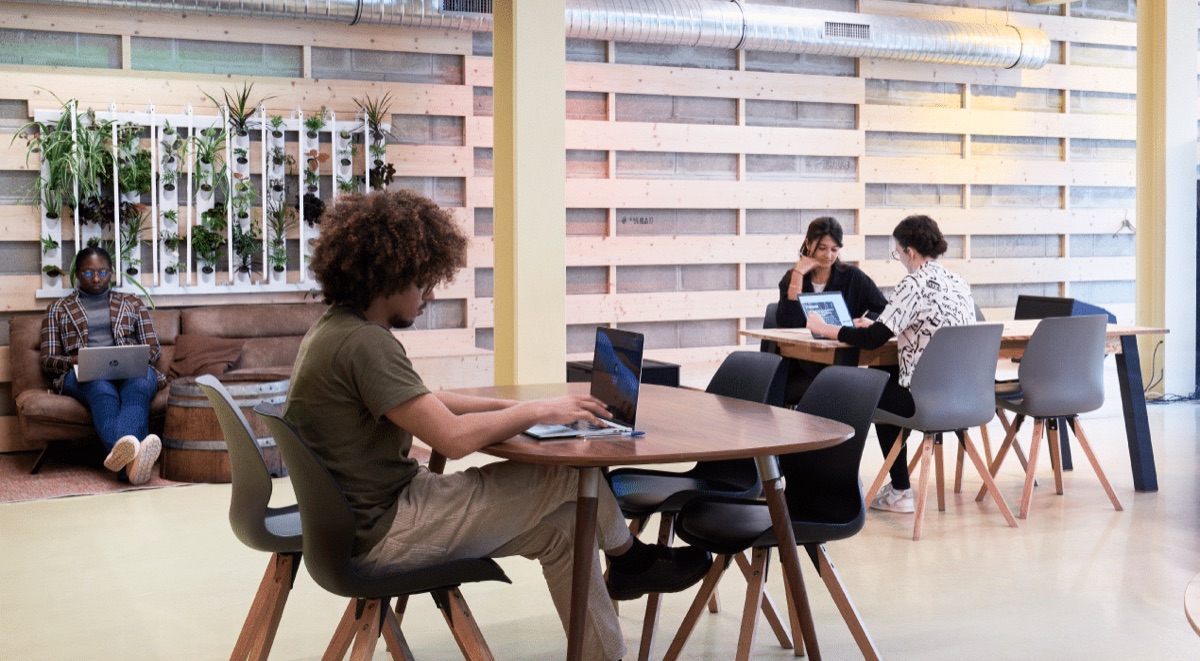 Espace de coworking de La Ruche à Paris : murs habillés de bois de palettes, mur végétal, canapé en cuir et grandes tables en bois où des membres travaillent sur ordinateur portable